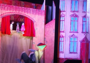 Pinokio patrzy na trzy pacynki, które występują w teatrze.