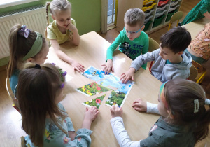 Dzieci przy stoliku układają puzzle "Wiosenna łąka".