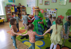 Dzieci tańczą w kole i śpiewają piosenkę pt. "Maszeruje wiosna". W środku koła gość, który odwiedził starszaków - pani Wiosna.