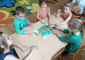 Dzieci przy stoliku układają puzzle "Wiosenna łąka".