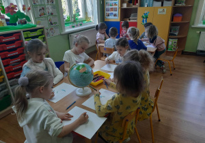 Dzieci przy stolikach wykonują plakat pt. "Dbam o Ziemię".