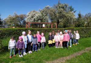 Przedszkolaki pozują w ogrodzie przedszkolnym na tle kwitnących drzew owocowych.