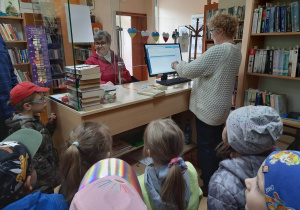 Pani bibliotekarka prezentuje dzieciom sposób wypożyczania książek.