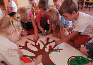 Dzieci przyklejają pociętą bibułę na szablon drzewa.