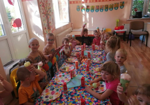 Dzieci siedzą przy stolikach przy słodkim poczęstunku.