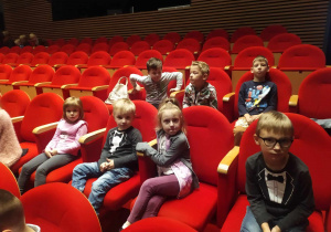 Grupa dzieci siedzi na krzesełkach na widowni w oczekiwaniu na przedstawienie.