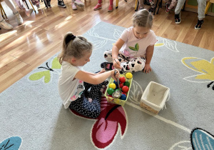 Dwie dziewczynki przekładają z jednego pudełka do drugiego piłeczki za pomocą łyżki wazowej.