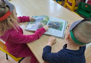 Dwoje dzieci ogląda przy stoliku książkę "Świat zwierząt", przedstawiającą ciekawostki z życia jeży.