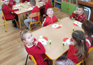Dzieci siedzą przy stoliku i wykonują postać Mikołaja.
