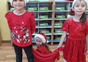 Dwie dziewczynki ciągną na kocu koleżankę w zabawie " Sanie Mikołaja"