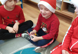 Chłopiec z zamkniętymi oczami trzyma w rękach przedmiot wyciągnięty z worka Mikołaja i odgaduje jego nazwę.