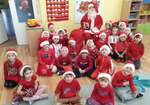 Dzieci w mikołajkowych czapkach na tle dekoracji z Mikołajem.