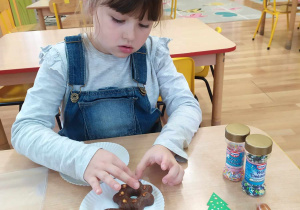 Dziewczynka ozdabia pierniczki cukrowymi pisakami i kolorową posypką.