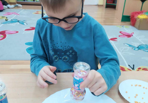Chłopiec ozdabia pierniczki cukrowymi pisakami i kolorową posypką.