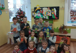 Przedszkolaki z prezentami na tle choinki i bożonarodzeniowej dekoracji.