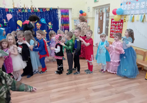 Dzieci w strojach karnawałowych tańczące na balu przedszkolnym.