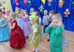 Dzieci w strojach karnawałowych tańczące na balu przedszkolnym.