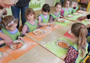 Przedszkolaki smarują pizzę sosem pomidorowym.