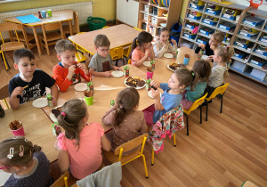 Grupa przy stoliku spożywa słodki poczęstunek.