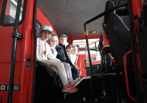 Dzieci siedzą w wozie strażackim.