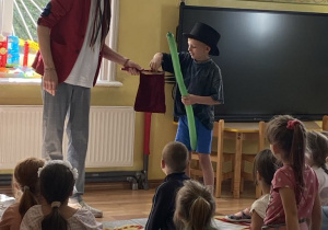 Chłopiec w magicznym kapeluszu wrzuca kilka balonów do magicznego worka, gdzie balony łączą się w jeden długi baon.