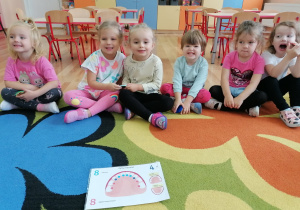 Dzieci siedzą na dywanie i słuchają na temat zębów mlecznych.