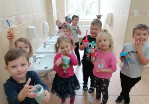 Dzieci stoją w łazience z kubkami i szczoteczkami po umyciu zębów.