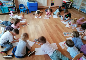Dzieci leżą na podłodze i rysują na swoich kartonach kropkę.
