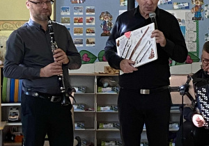 Pan Maciek trzyma książkę i pokazuje dzieciom rodzinę klarnetów. Obok drugi muzyk prezentuje klarnet..