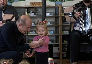 Pan Maciek podaje dziewczynce z grupy maluszków batutę do ręki.