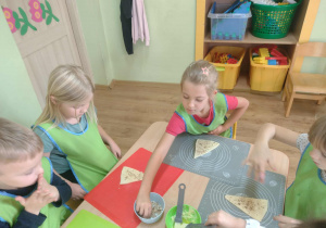 Dzieci posypują swój kawałek ciasta orzeszkami.