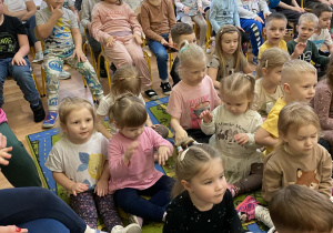 Przedszkolaki siedzą na krzesełkach i słuchają gry na djembe.