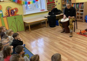 Muzyk gra na djembe. Dzieci z zainteresowaniem słuchają jego brzmienia.