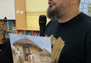 Pan Michał trzyma w ręce zdjęcie przedstawiające dom afrykański i opowiada z czego jest zbudowany.