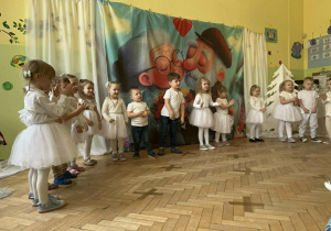 Grupa dzieci ubrana na biało , stoi w rzędzie i śpiewa piosenkę "Powitanie Babci i Dziedka"