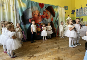 Dziewczynka i chłopczyk do mikrofonu recytują wiersz dla babci i dziadka.