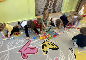 Grupa dzieci liczy guziki i układa je w odpowiedniej ilościo pod narywowanymi kropkami.