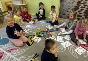 Dzieci układają guziki na liniach, które tworzą figury geometryczne.