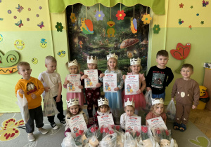 Zdjęcie przedstawia grupę dzieci. Dziewczynki trzymają dyplomy, [rzed nimi stoją upominki. Chłopcy w rękach trzymają reklamówki z upominkami.