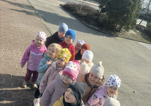 Zdjęcie przedstawia grupę dzieci idących na spacer. Dzieci ustawione są parami. W tle widać jezdnię oraz drzewa.