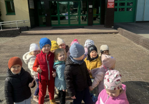 Zdjęcie przedstawa grupę dzieci. Za nimi widoczny jest budynek Państwowej Straży pożarnej.