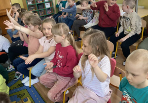 Dzieci siedzą na krzesełkach i dyrygują rękami do utworu Mozarta.