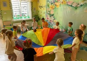 Dzieci trzymają chustę animacyjną, po której turla się piłka.