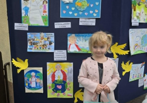 Antosia stoi z nagrodą na tle wystawy prac konkursowych.
