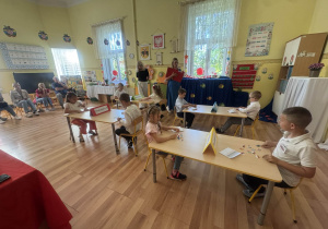 Dzieci siedzą przy stolikach. Na stoliku widzimy rozłożone flagi państw europejskich.