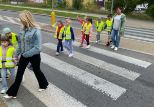 Grupka dzieci z dwoma paniami przechodzi przez przejście dla pieszych.