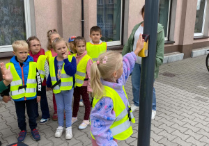 Dziewczynka włącza przycisk przy sygnalizatorze świetlnym w celu przejścia na drugą stronę.
