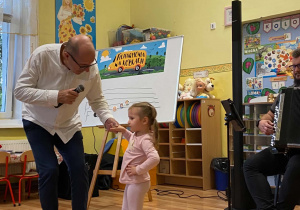 Prowadzący trzyma za rękę dziewczynkę z najmłodszej grupy i okręca ja w tańcu.