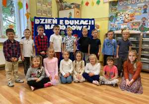 Grupa Biedronki pozuje do zdjęcia na tle dekoracji z napisem Dzień Edukacji Narodowej.