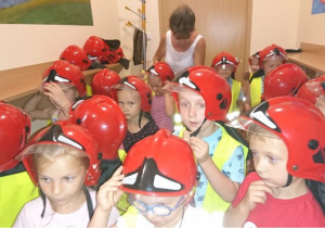 Grupa dzieci z hełmami strażackimi na głowach.